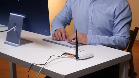 It technician connecting an ethernet cable to a wireless router at a desktop Stock Footage 348447543