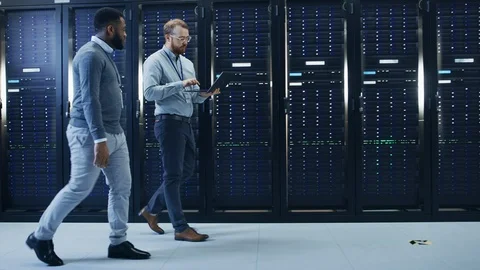 IT Technician with a Laptop Computer and Black Male Engineer Colleague Talk Stock Footage 100804160