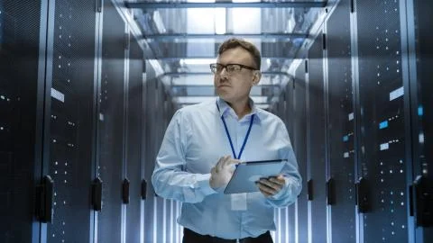 IT Technician Walks Through Rows of Server Racks in Data Center. Simultaneous Stock Photos