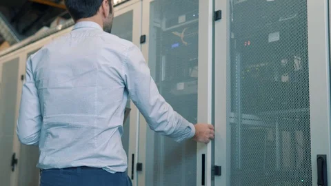 IT Technician Working On A Laptop Standing Before Open Server Rack Cabinet. 库存影片 103211912