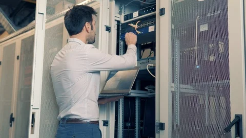 IT Technician Working On A Laptop Standing Before Open Server Rack Cabinet. 库存影片 103211931
