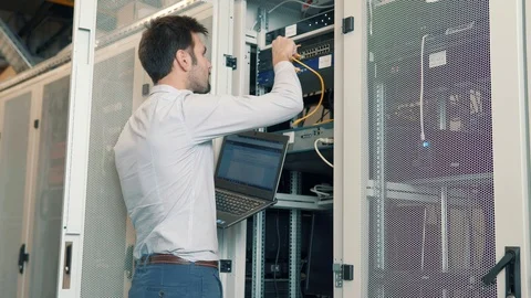 IT Technician Working On A Laptop Standing Before Open Server Rack Cabinet. 库存影片 103211971