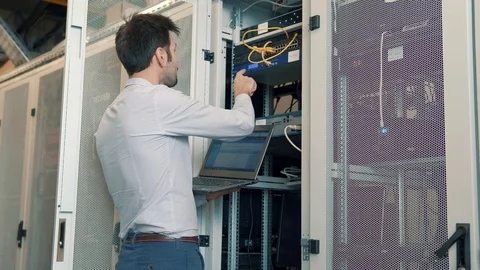 IT Technician Working On A Laptop Standing Before Open Server Rack Cabinet. 库存影片 103212005