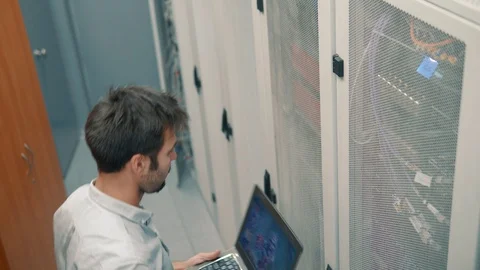 IT Technician Working On A Laptop Standing Before Open Server Rack Cabinet. 库存影片 103213839