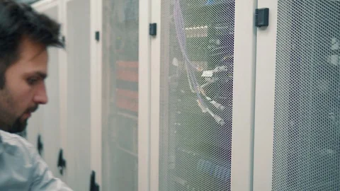 IT Technician Working On A Laptop Standing Before Open Server Rack Cabinet. 库存影片 103214115