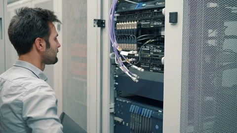 IT Technician Working On A Laptop Standing Before Open Server Rack Cabinet. 库存影片 103214249