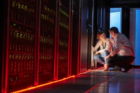 IT technicians talking at glowing panel in dark server room Foto stock