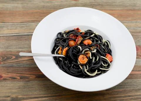 Italian black spaghetti, alla Veneziana, with grilled prawns and dried tomato Stock Photos
