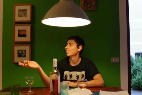 An Italian boy gesticulates while talking to friends at a table drinking wine Stock Photos