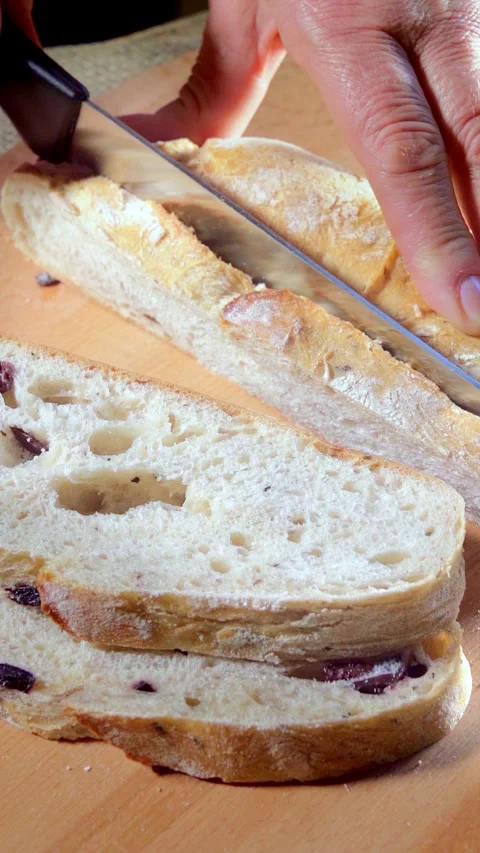 Italian bread with olives. Cutting bread into slices on a wooden cutting board. Stock Footage 295368903
