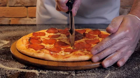 Italian chef cuts a pepperoni pizza into even pieces on a wooden stand. Stock Footage 130974953