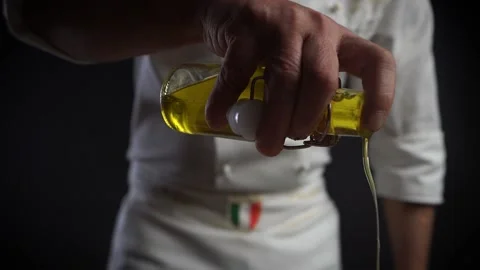 Italian chef in the kitchen in a white robe pours yellow olive oil over a dish. Vidéo 143420105