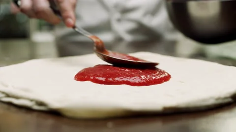 Italian chef in a pizzeria using a spoon to pour tomato sauce onto the dough to Stock Footage 199458252