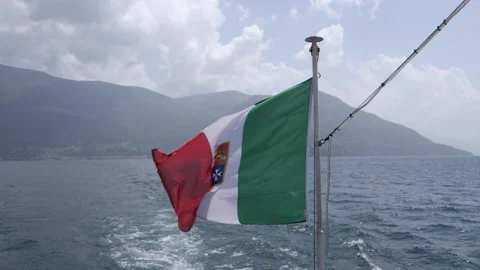 Italian flag waving in the wind in front of a big mountain in the lake maggiore Video stock 156748183
