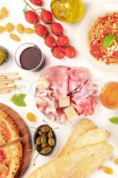 Italian food. Pizza, pasta, cheese, ham, capers, wine, tomatoes, overhead shot Stock Photos