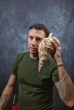 Italian man hears a large shell coming up to his ear Stock Photos