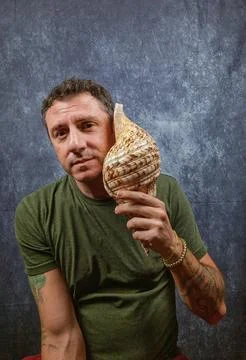 Italian man hears a large shell coming up to his ear Stock Photos