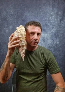 Italian man hears a large shell coming up to his ear Stock Photos