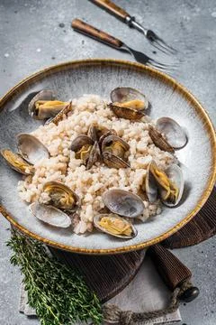 Italian Risotto with clams in a rustic plate with herbs. Gray backgroud. Top Stock Photos