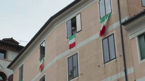Italy flags swinging in the wind with one woman looking outside the window Stock Footage 130588080