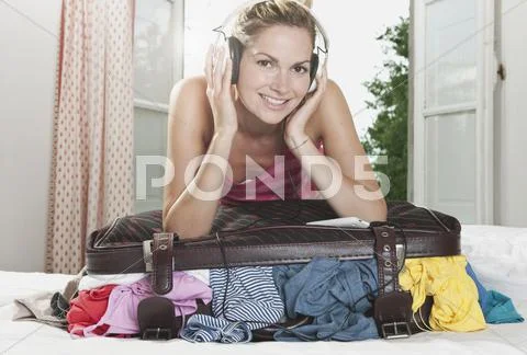 Italy, Tuscany, Young woman listening to music on top of stuffed suitcase in Stock Photos