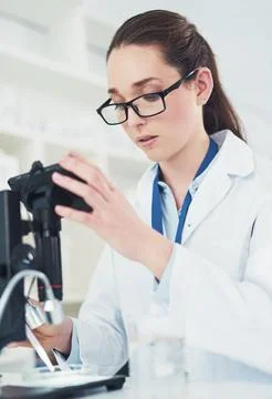 Its all about the small things. a focused young female scientist looking through Stock Photos