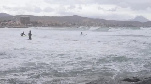 It's a cloudy day and surfers in wetsuits are trying to lie down on a board in Stock Footage 303409832