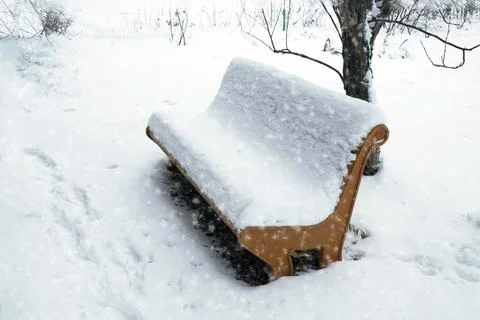 It's winter, it's snowing. The park bench is covered with snow Stock Photos