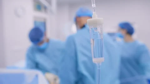 IV Drip Bottle in Focus with Surgical Team Working in Background During Oper Stock Footage 308420074