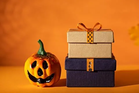 Jack-o-lantern beside stacked gift boxes on orange background for Halloween.. Stockfoto's