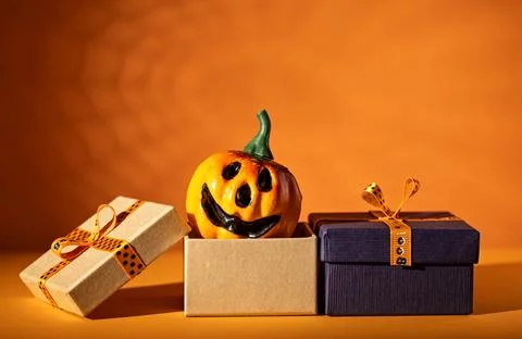 Jack o lantern emerging from gift box between wrapped presents on orange ba.. Stock Photos