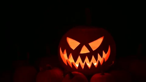 Jack-o-lantern with inner light shines among small orange pumpkins Stock Footage 317984000