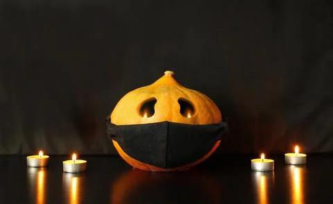 Jack-o-lantern pumpkin with face drawn on black protective mask Stock Photos