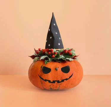 Jack o lantern pumpkin head with flowers in black witch hat on beige Stock Photos