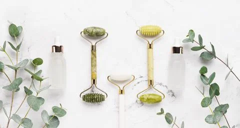 Jade face rollers, dropper bottles and eucalyptus branches on a white marble Stock Photos