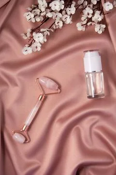 Jade roller and cometic product on shiny pink fabric. Stock Photos