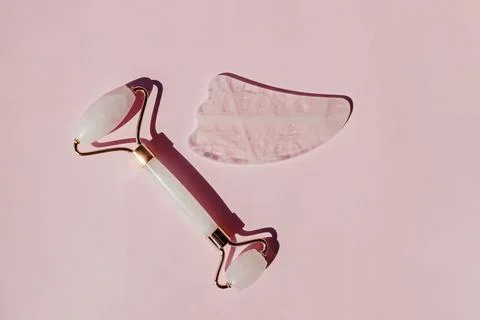Jade roller and gua sha massage tool on pink background Stock Photos