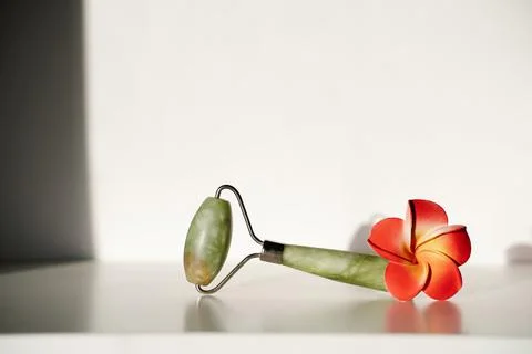 Jade roller on white background with red flower Stock Photos