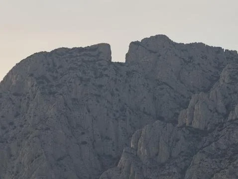 Jagged cliffs under dusky sky, dusk reveals sharp rocky faces and ancient Stock Photos