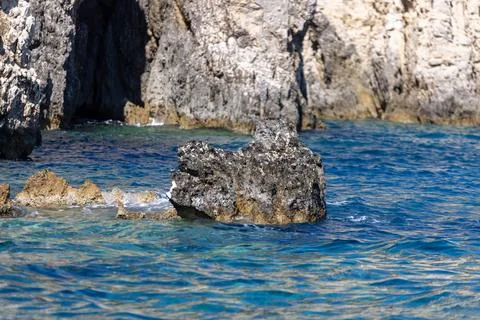 Jagged dark rocks surrounded by clear turquoise and blue Ionian Sea water b.. Stock Photos