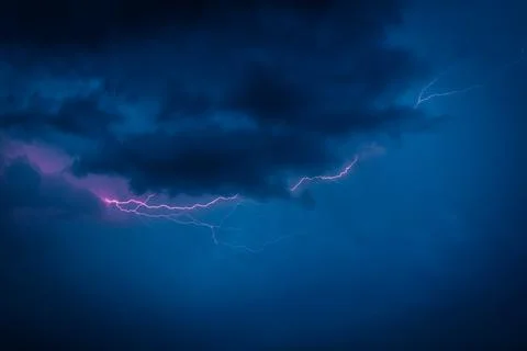 A jagged lightning bolt cuts through dark storm clouds in a vivid blue night sky Stock Photos