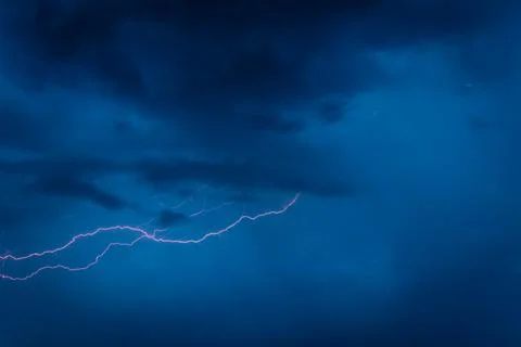 A jagged lightning bolt cuts through dark storm clouds in a vivid blue night sky Stock Photos