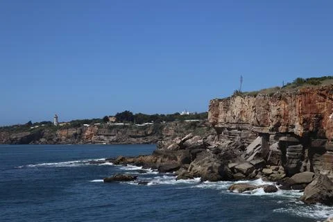 Jagged limestone cliffs of Cascais with lighthouse in the distance Stock Photos