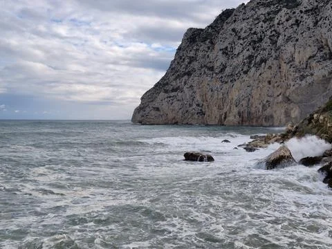 Jagged limestone face with foaming waves beneath stormy sky showcasing natural Stock Photos