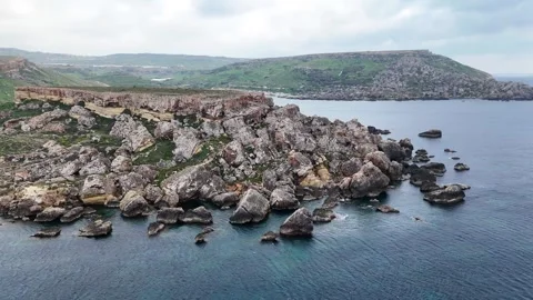 Jagged rock stacks dot the shallows off a reddish headland on maltas coast sea Stock Footage 343581543