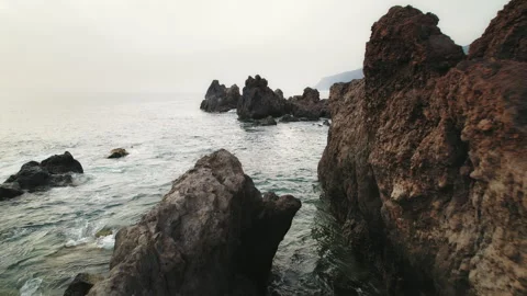 Jagged rocks facing the ocean, the misty cliffs in the distance and the rugged Stock Footage 308260900