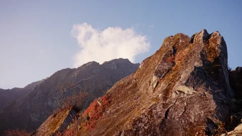Jagged rocky mountain peak rises beside a single drifting cloud Stock Footage 344177849