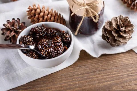 Jam from young pine cones in white bowl with cones and jar on white kitchen t Stock Photos