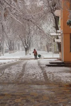 Janitor or sweeper in orange jacket cleaning city streets from snow with shovel Stock Photos
