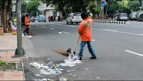 A janitor is working to sweep the garbage on the city street Stock Footage 303570742